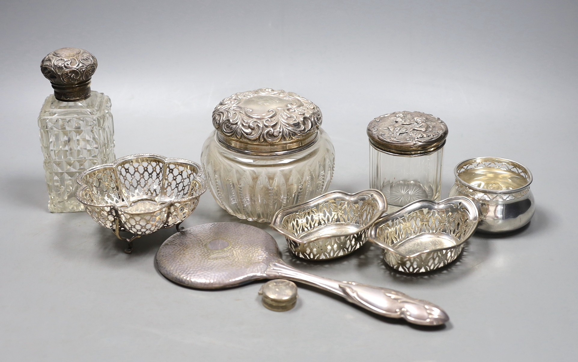 A small pair of George V pierced silver bonbon dishes, 92mm, two small pierced silver bowls, a modern silver pill box, three silver mounted glass toilet jars and a silver plated hand mirror.